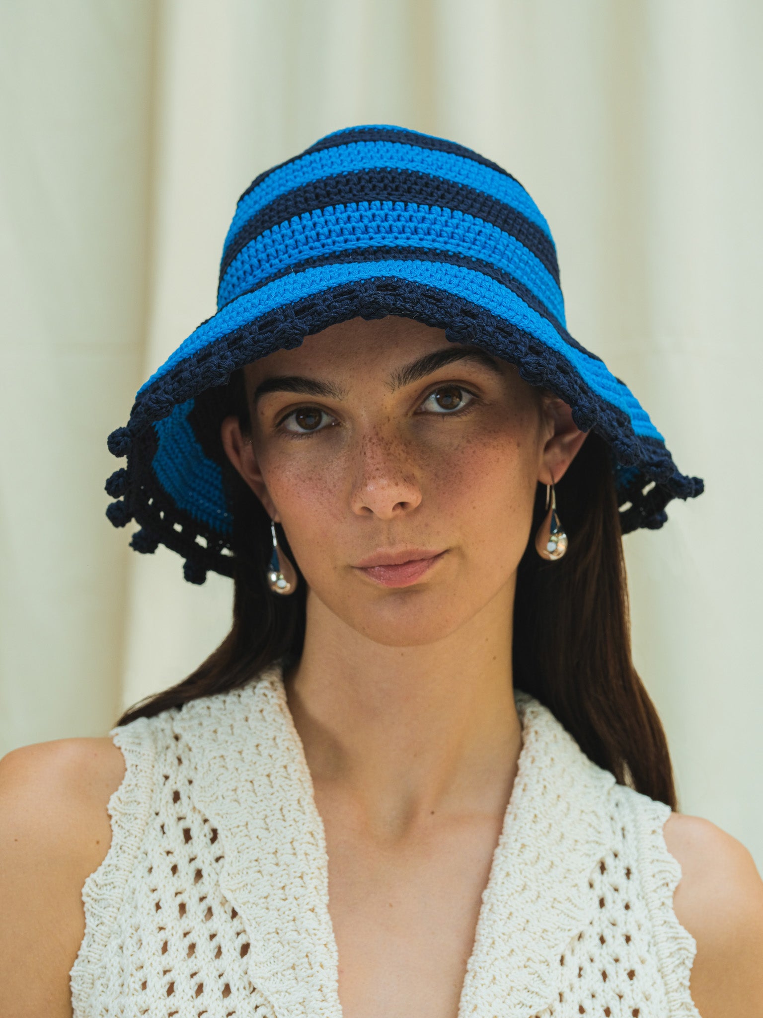 Front view of hand crocheted wide brim sun hat in cerulean and navy stripe with pom pom trim
