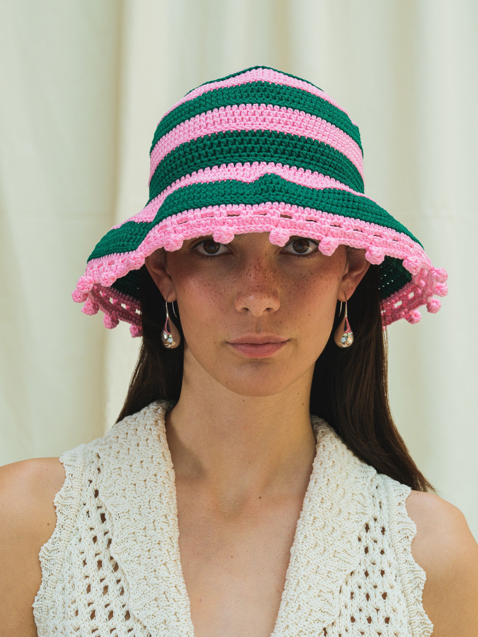 Front view of hand crocheted wide brim sun hat in peony pink and dark emerald stripes with pom pom trim