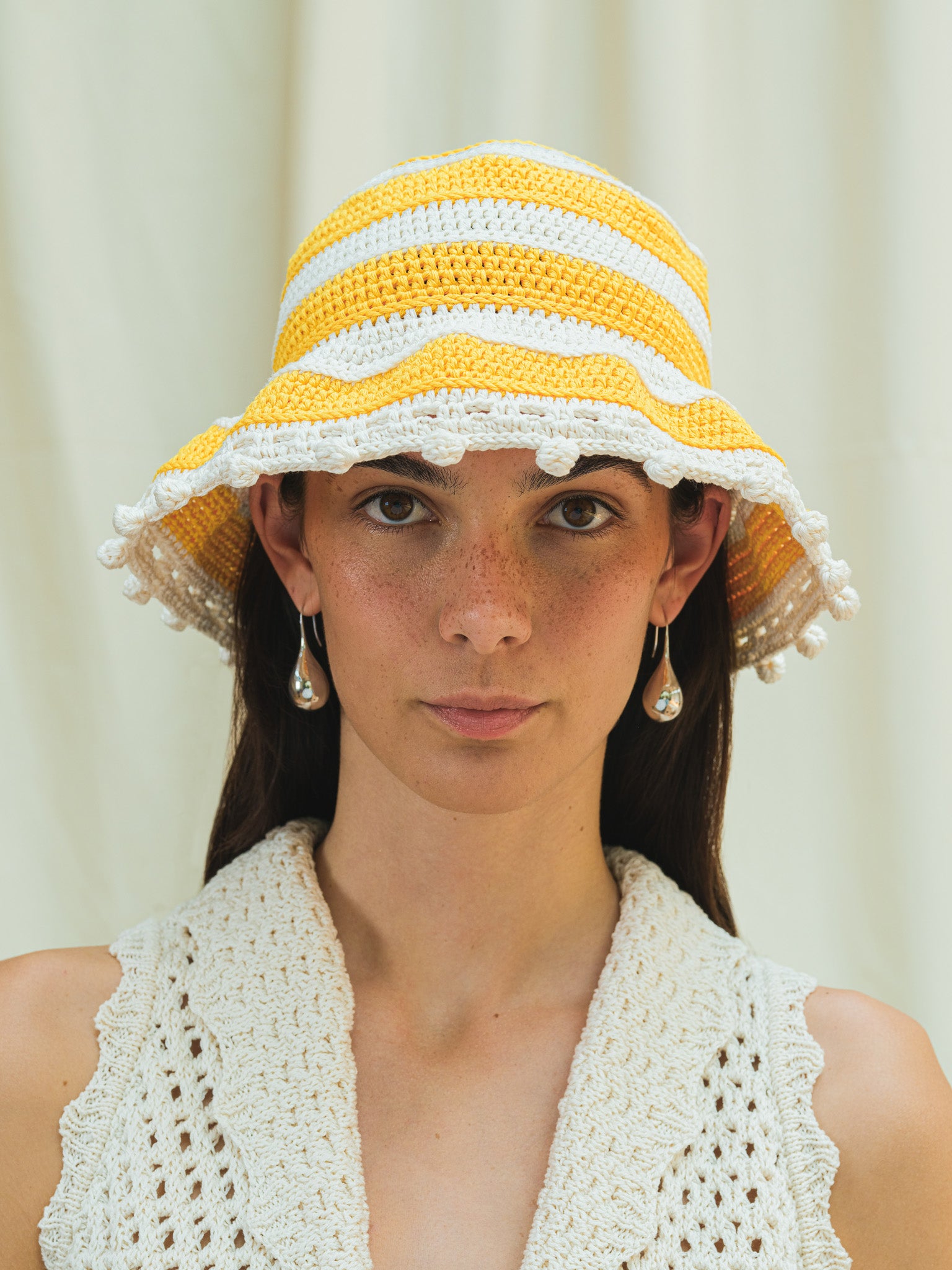 Front view of hand crocheted wide brim sun hat in linen white and capri yellow stripes with pom pom trim