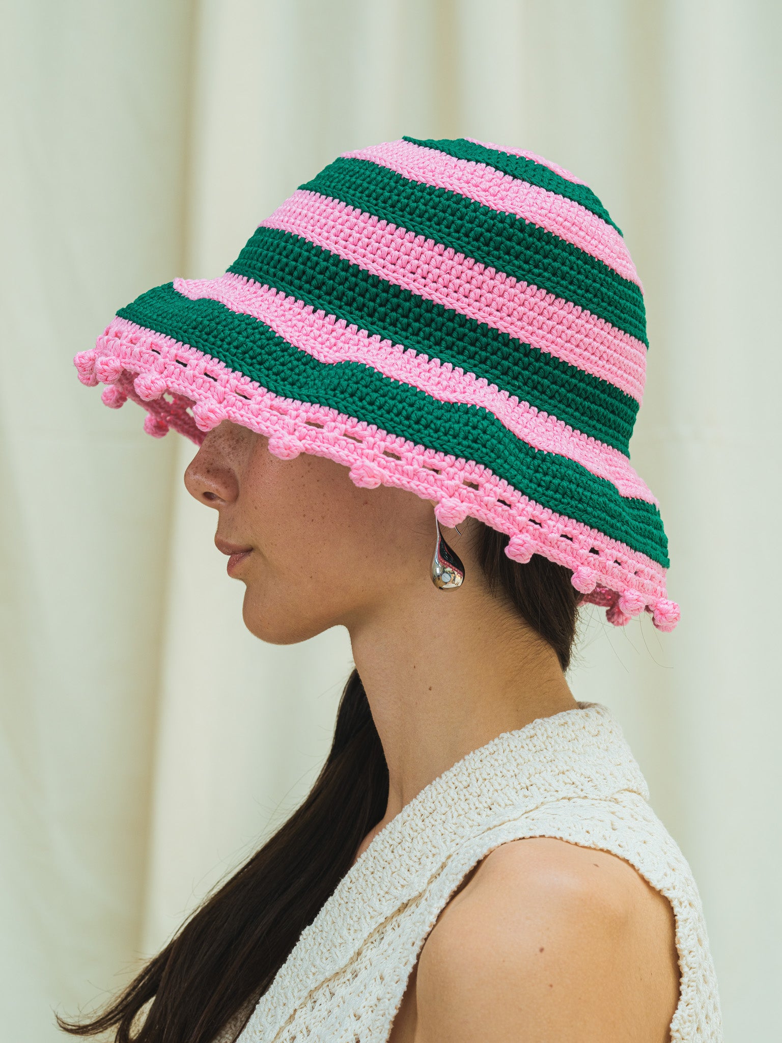 Side view of wide brim sun hat in peony pink and dark emerald stripes with pom pom detail