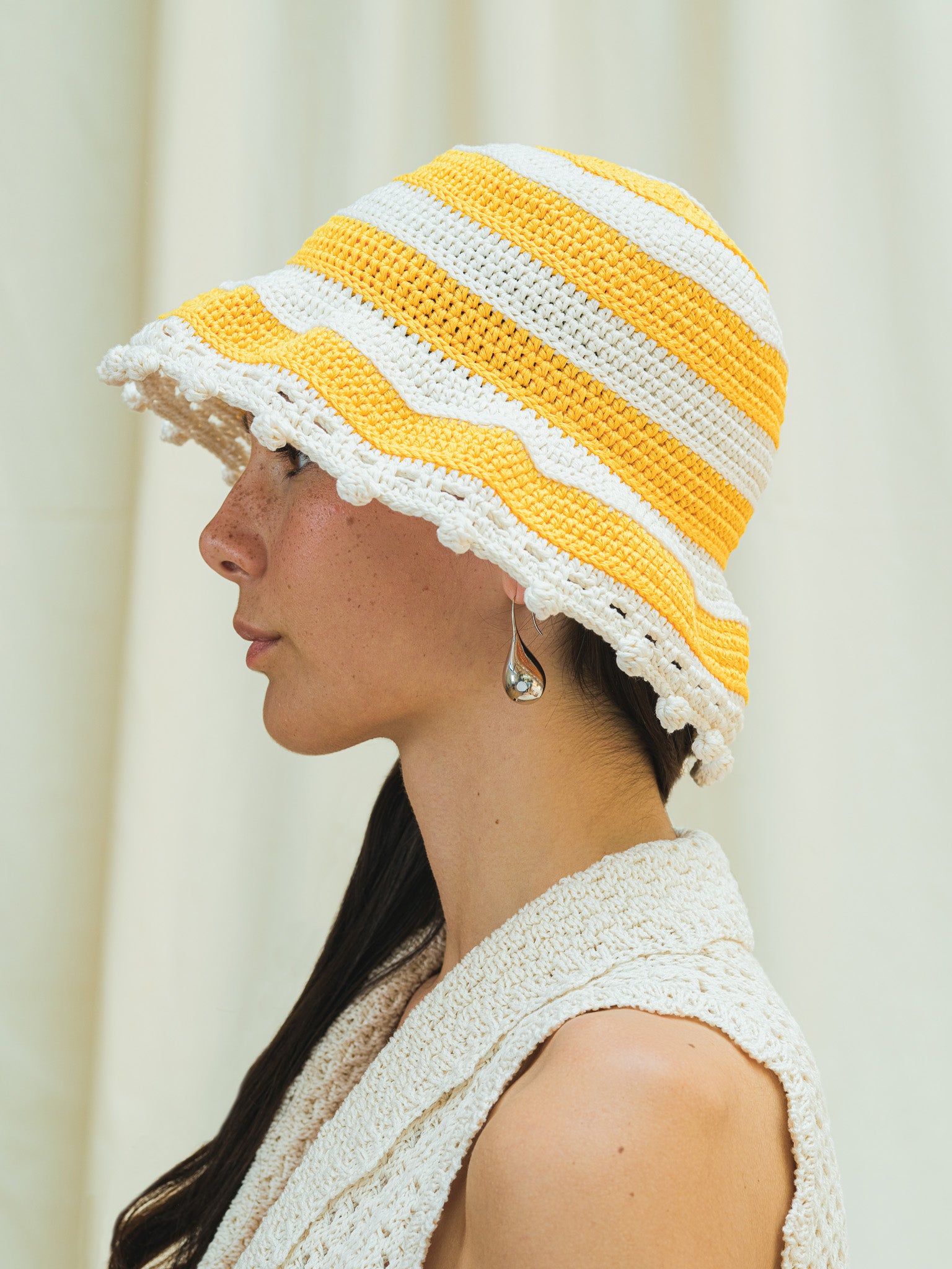 Side view of wide brim sun hat in linen white and capri yellow stripes with pom pom detail