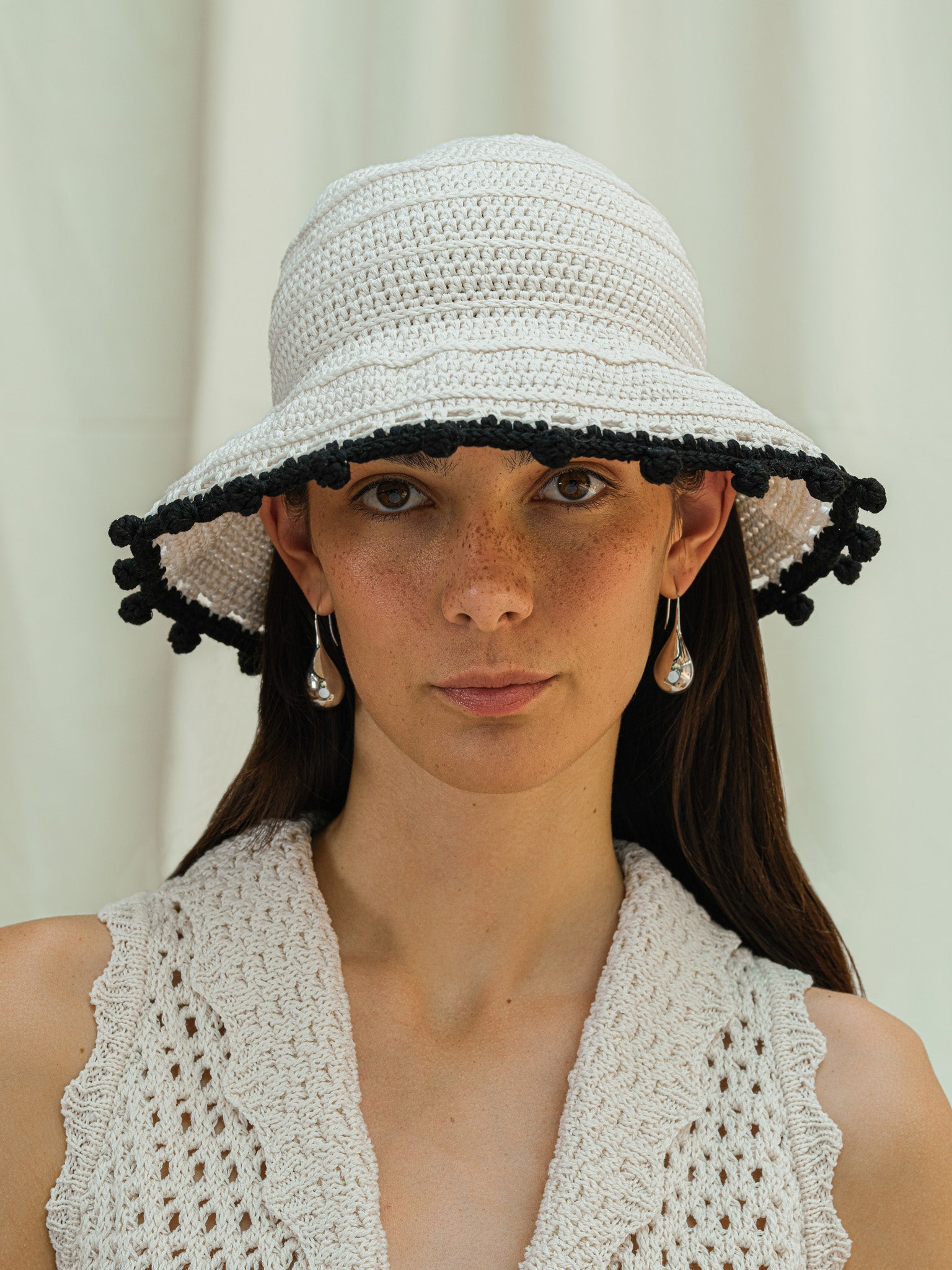 Front view of hand crocheted wide brim sun hat in linen white with black pom pom trim