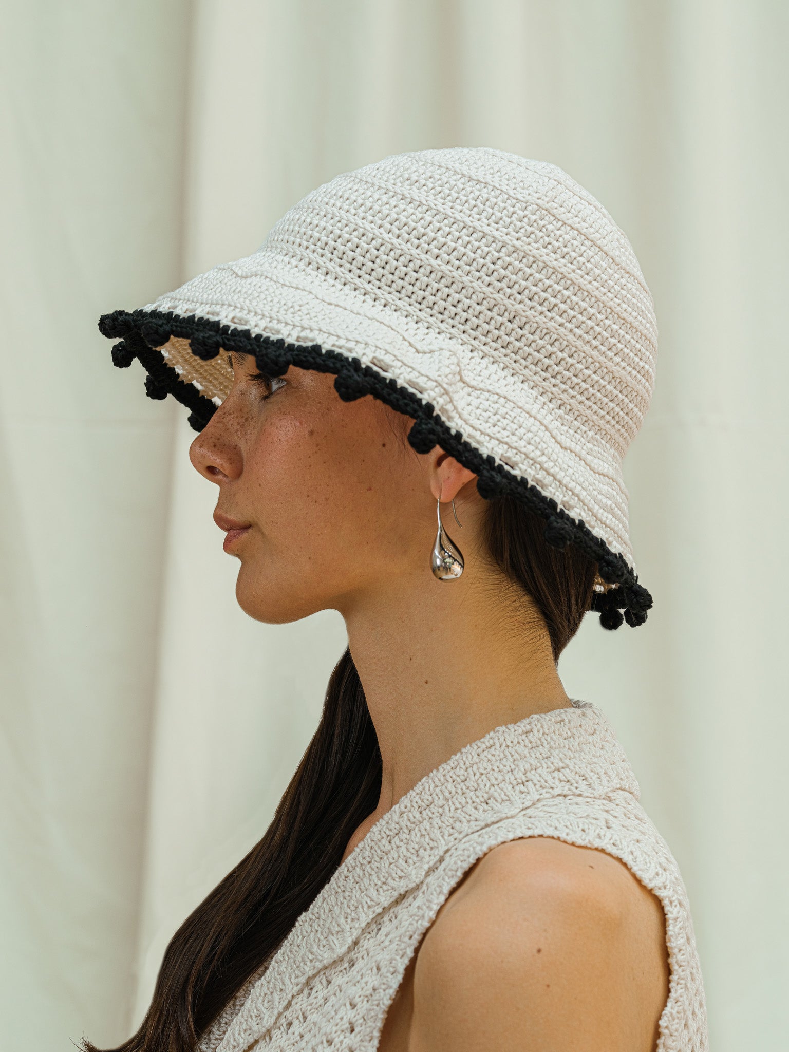 Side view of linen white wide brim sun hat with black pom pom detail